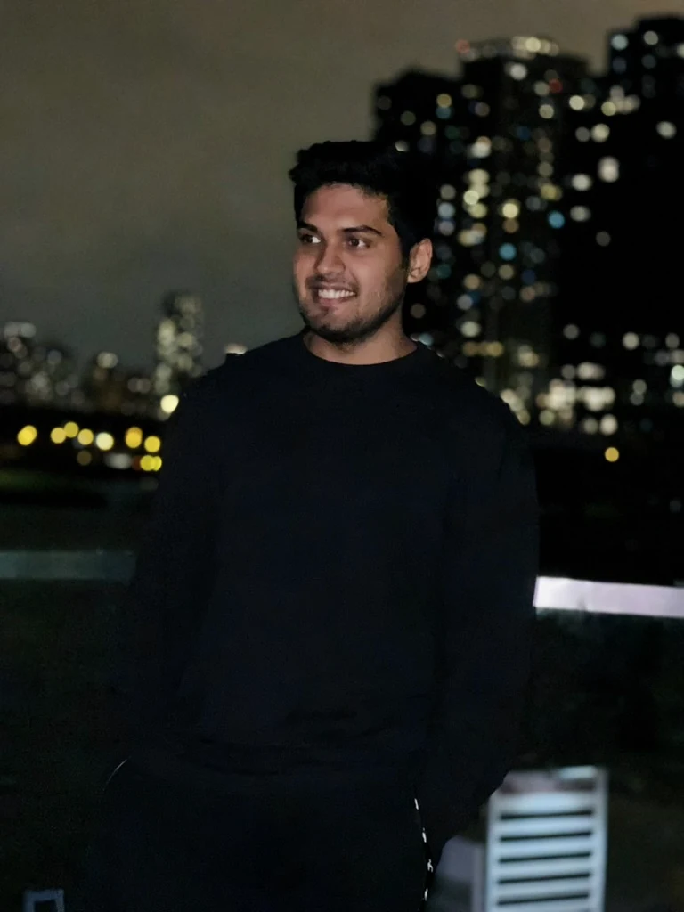 Jamal smiling on a rooftop at night, city lights behind him